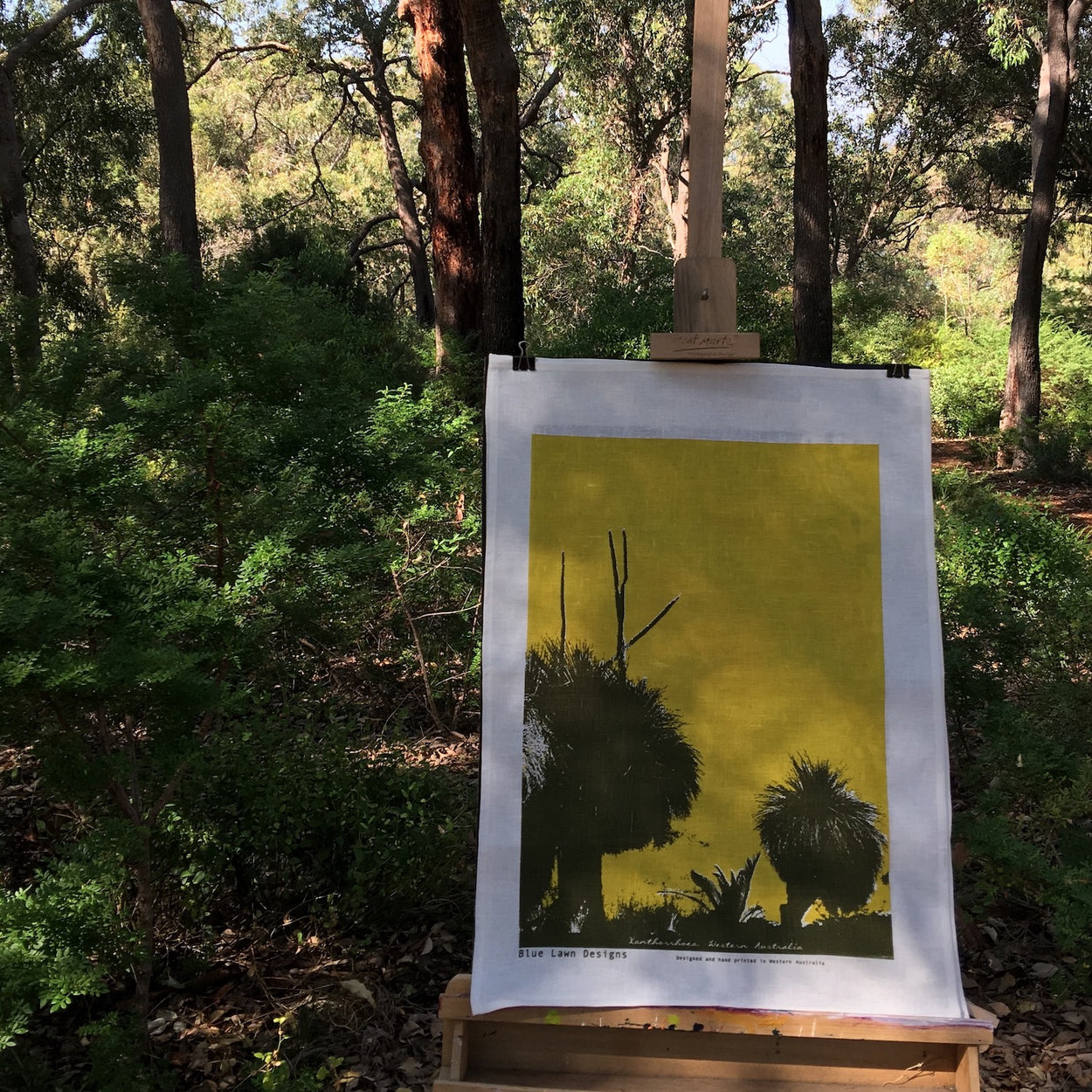 Photograph of a grass trees tea towel on an easel in the forest.